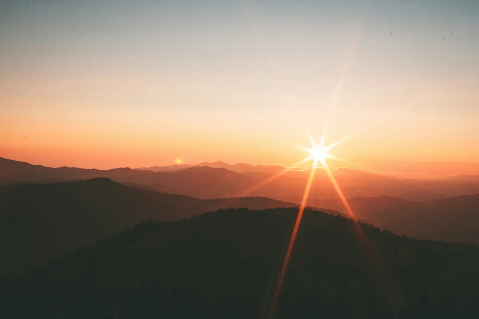 Nascer do sol entre serras encadeadas, com os raios abrindo em estrela sobre o horizonte