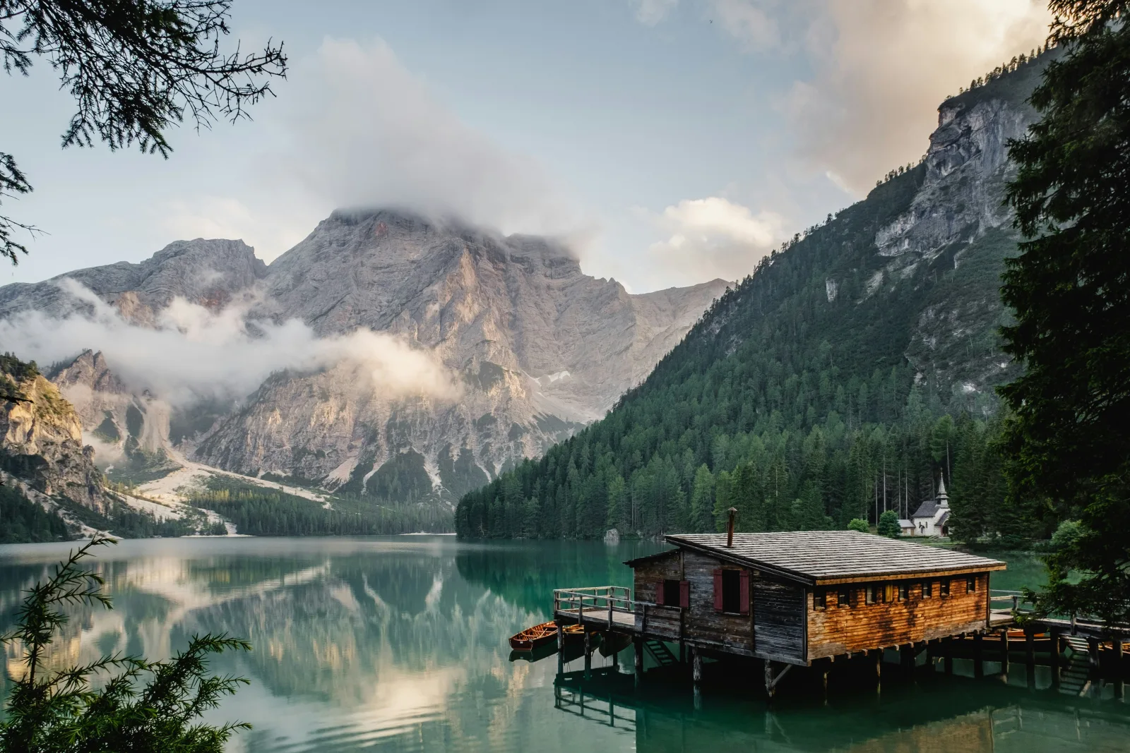 Casa de madeira sobre palafitas na margem de um lago de montanha, com um barco a remo ancorado