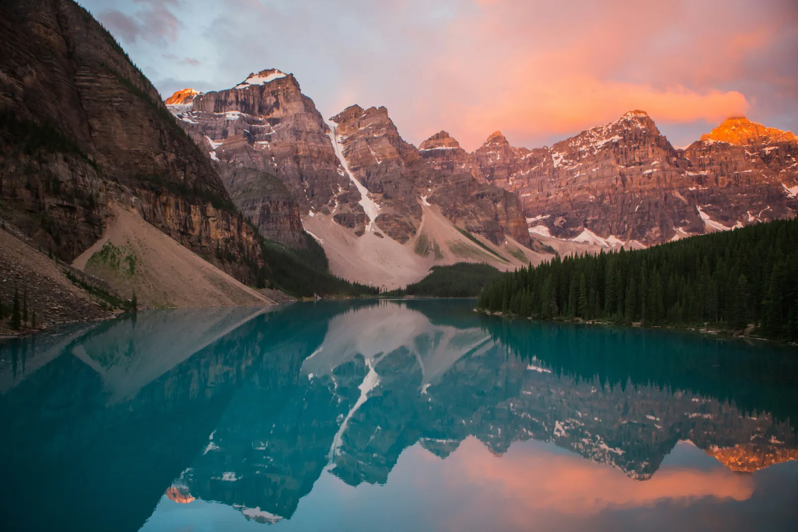 Lago espelhado refletindo picos nevados sob um céu rosado no fim da tarde