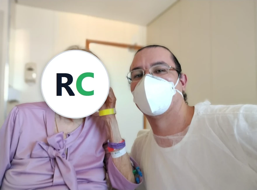 Fisioterapeuta ao lado de uma idosa sentada num quarto de hospital
