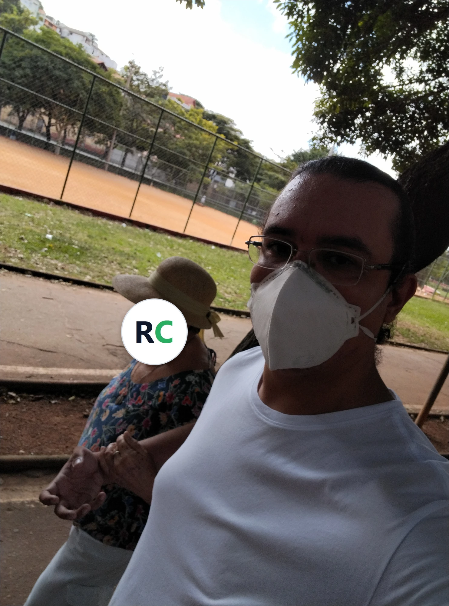Fisioterapeuta caminhando de braço dado com uma idosa de chapéu, numa praça