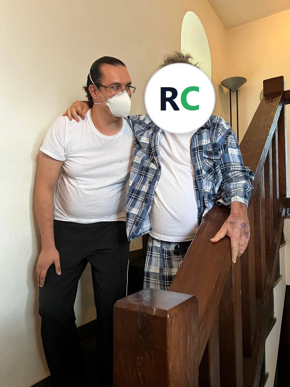 Fisioterapeuta no alto de uma escada de madeira, com o braço de um idoso apoiado no ombro dele
